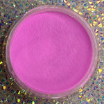 Bright pastel hot pink dip powder in clear round container on holographic surface.