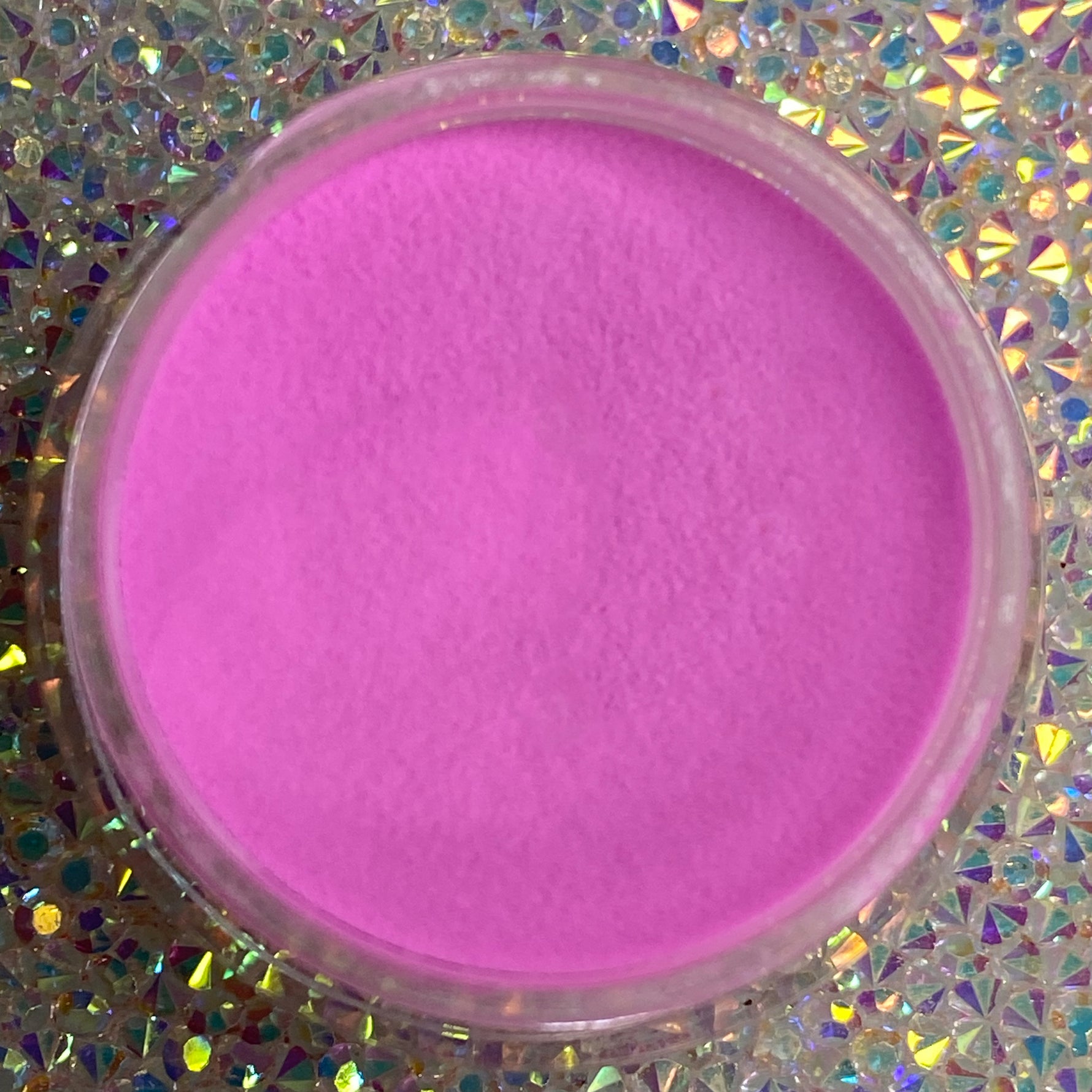 Bright pastel hot pink dip powder in clear round container on holographic surface.
