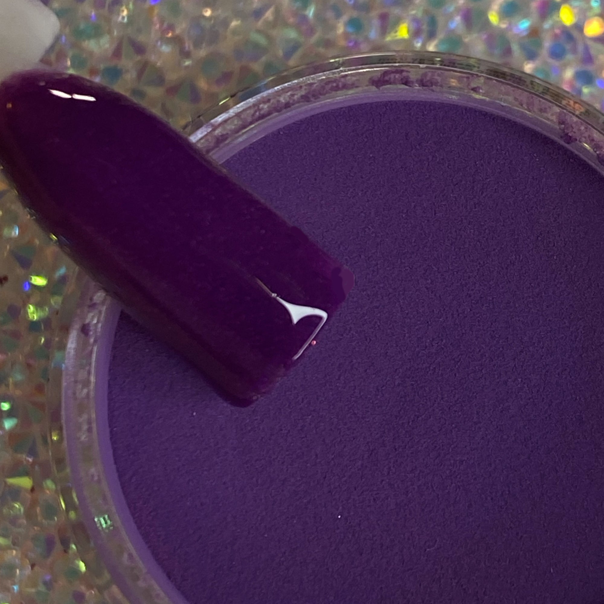 Deep purple dip powder with smooth, matte finish swatched on nail tip over open jar.