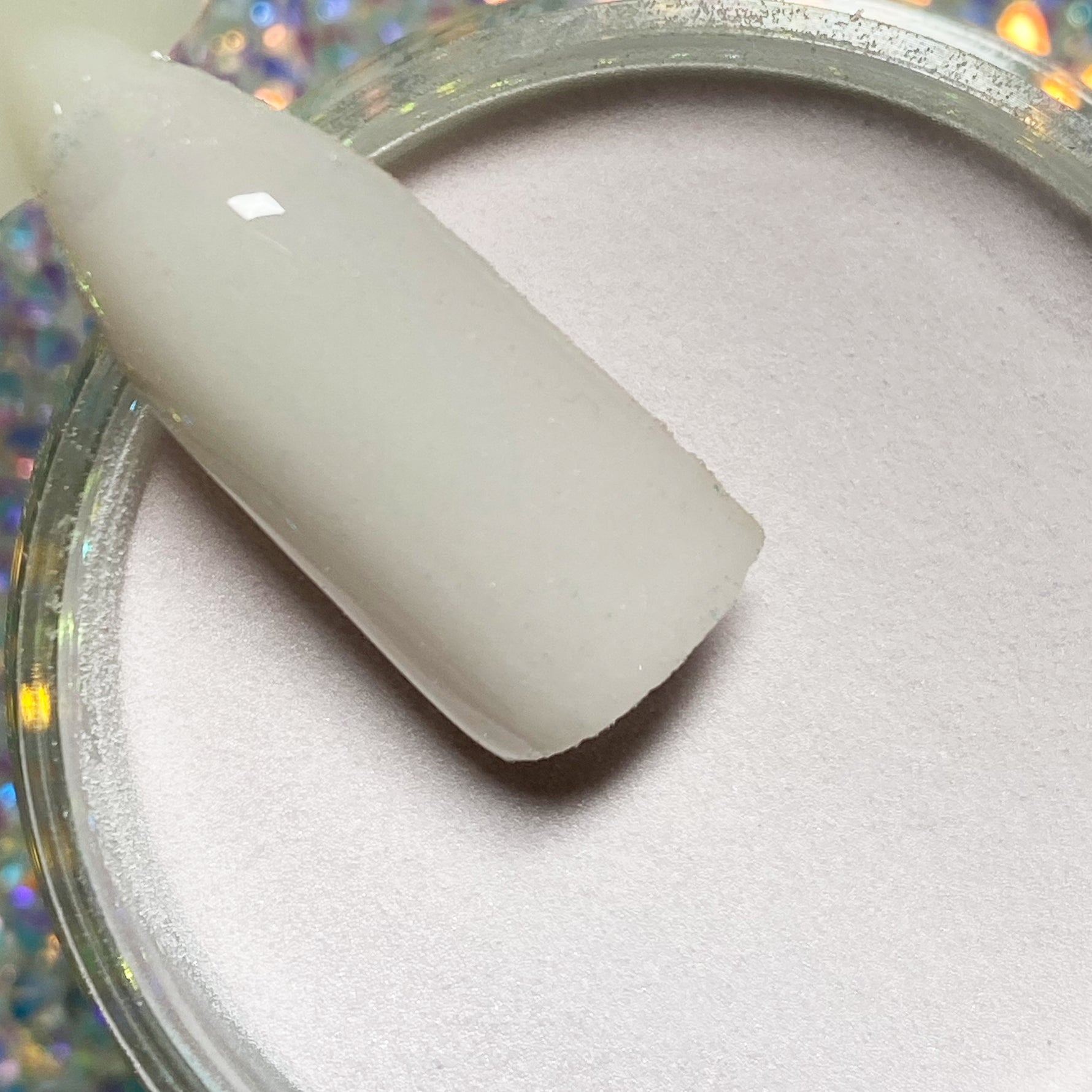 Smooth beige nude dip powder on a nail swatch stick above an open jar of powder.