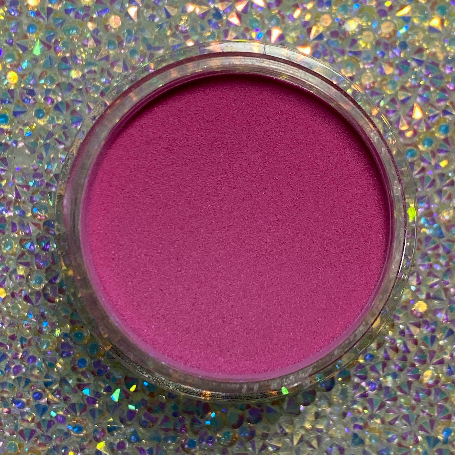 Open jar of vibrant hot pink dip powder on iridescent glitter background.