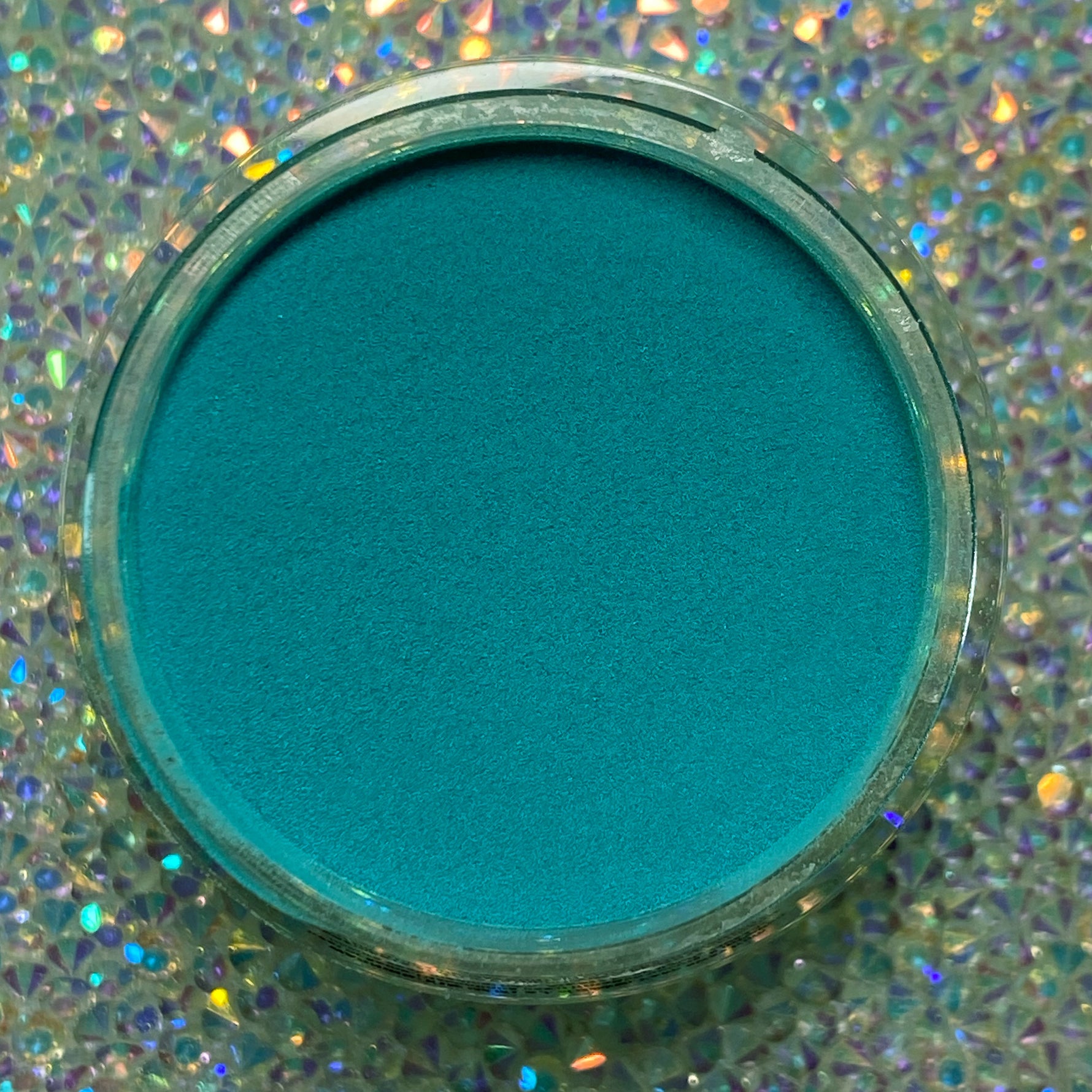 Open jar of vibrant teal dip powder on a sparkling holographic background.