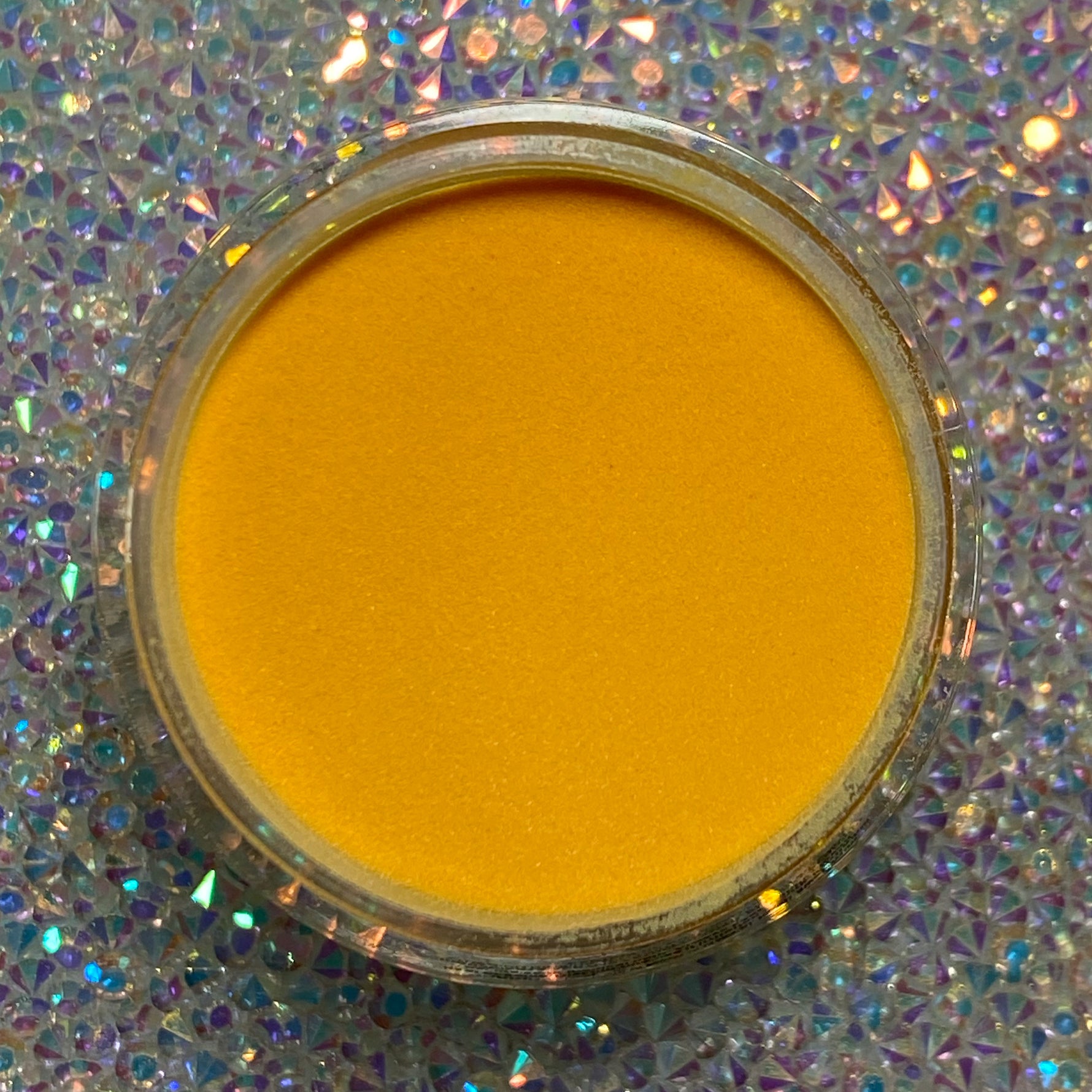 Bright yellow-orange dip powder in a round clear container on a sparkling iridescent surface.
