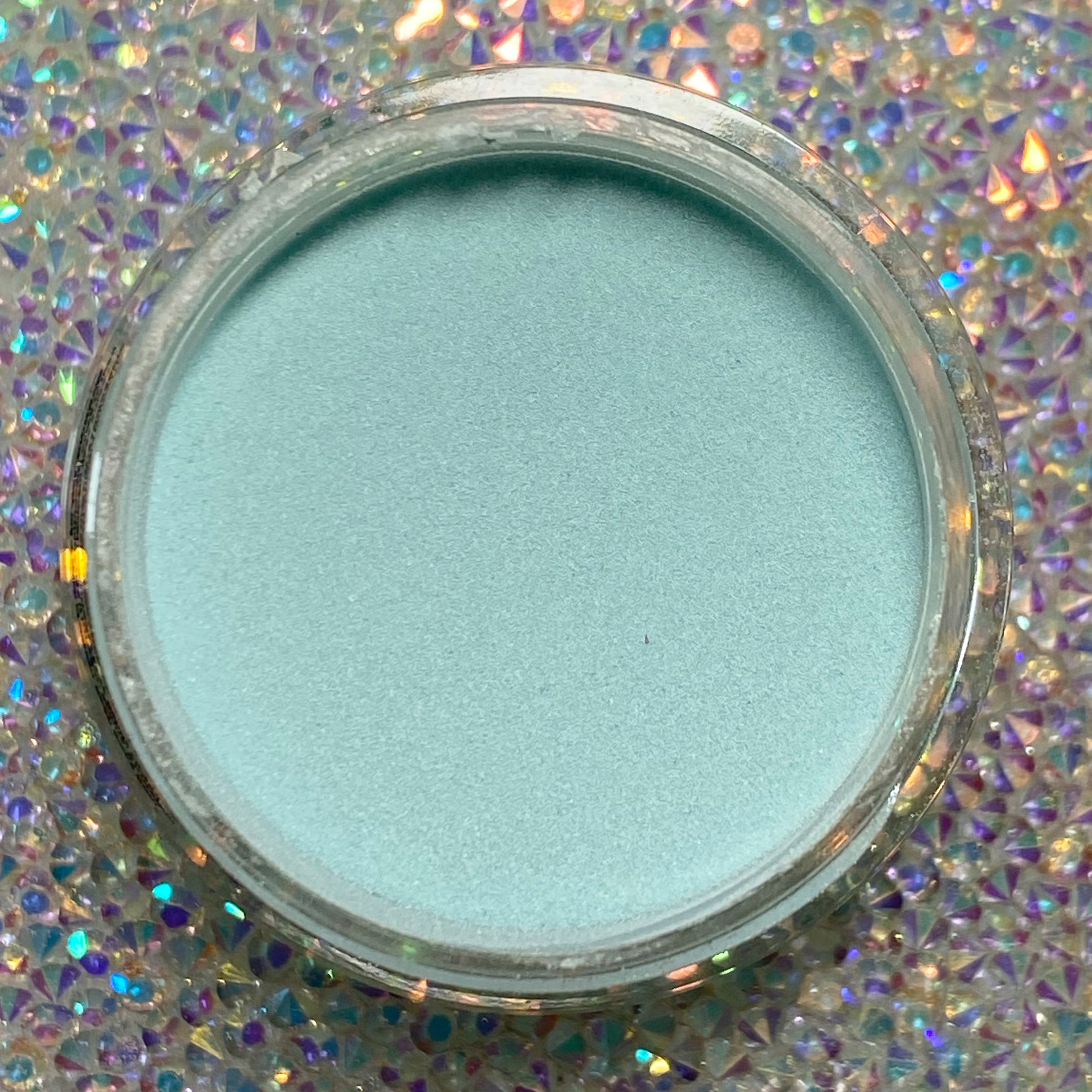 Light pastel blue dip powder in clear round jar with iridescent glitter background.