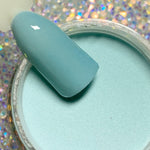 Open jar of smooth, pastel blue dip powder with matching nail tip above it.