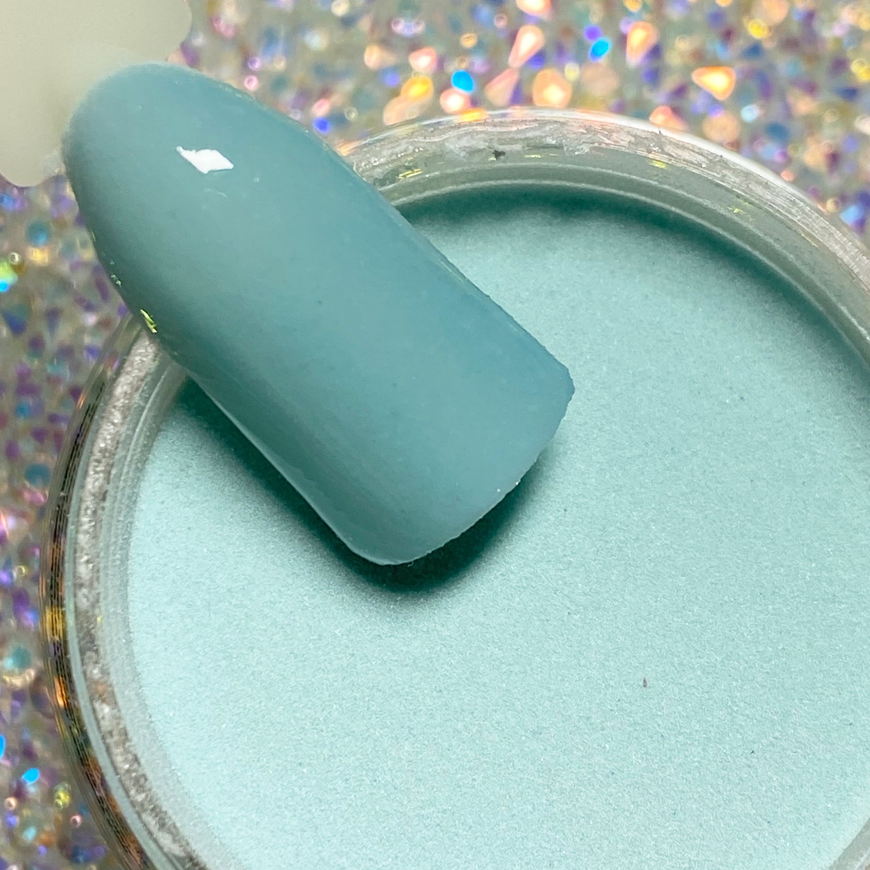 Open jar of smooth, pastel blue dip powder with matching nail tip above it.