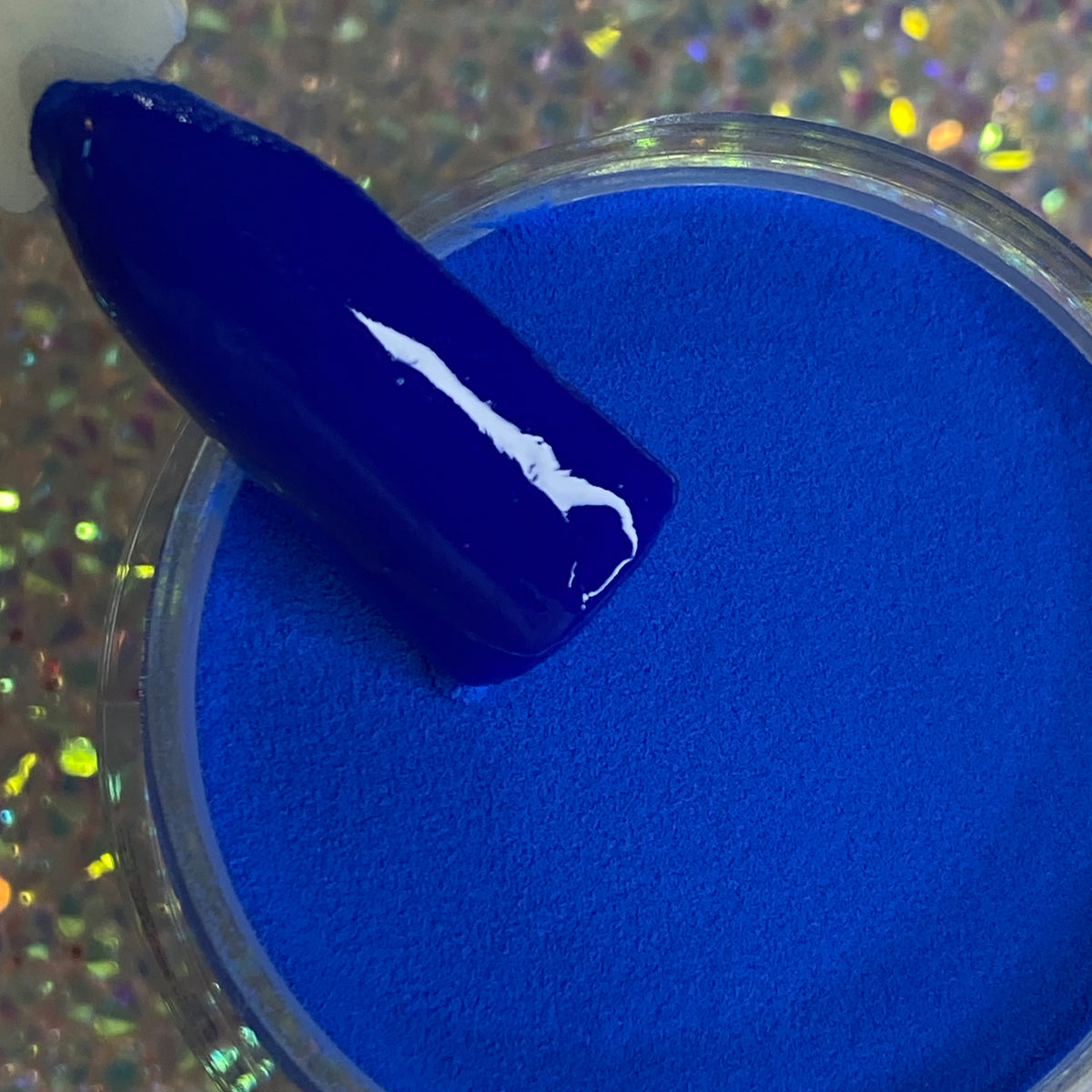 Bright royal blue solid dip powder with glossy nail tip sample on iridescent background.