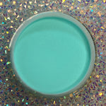 Round container of smooth teal dip powder nail polish on iridescent holographic background.