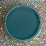 Open container of deep blue dip powder nail polish on iridescent holographic surface.
