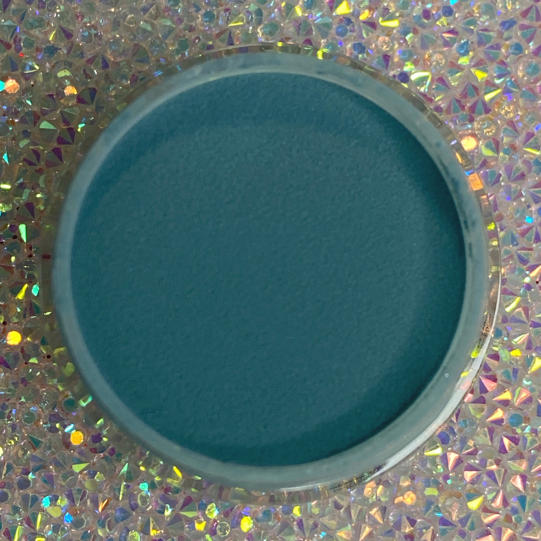 Open container of deep blue dip powder nail polish on iridescent holographic surface.