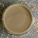 Open container of smooth tan dip powder nail polish on holographic surface.
