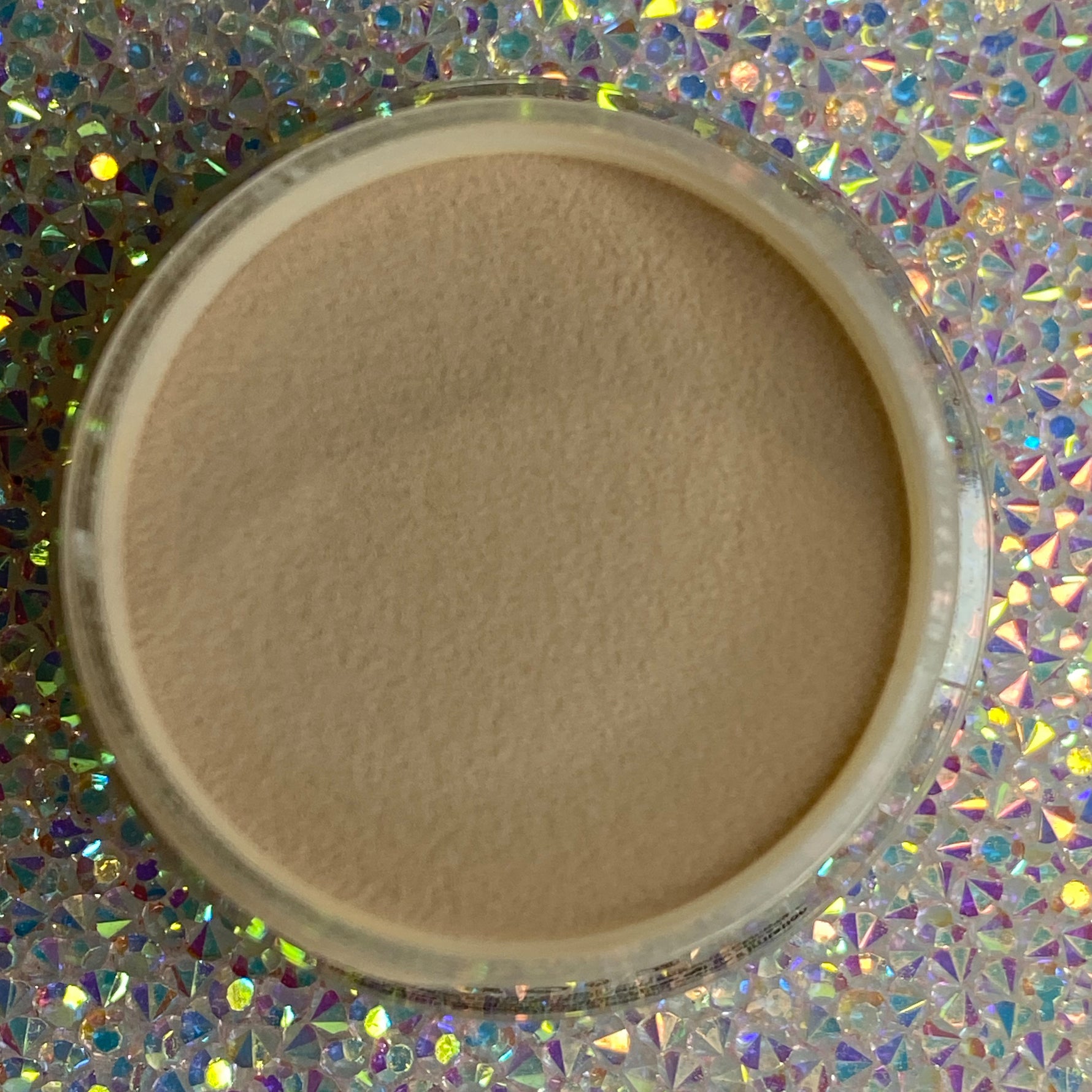Open container of smooth tan dip powder nail polish on holographic surface.