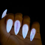 Long almond-shaped nails with white glow-in-the-dark polish and purple heart designs on two nails.