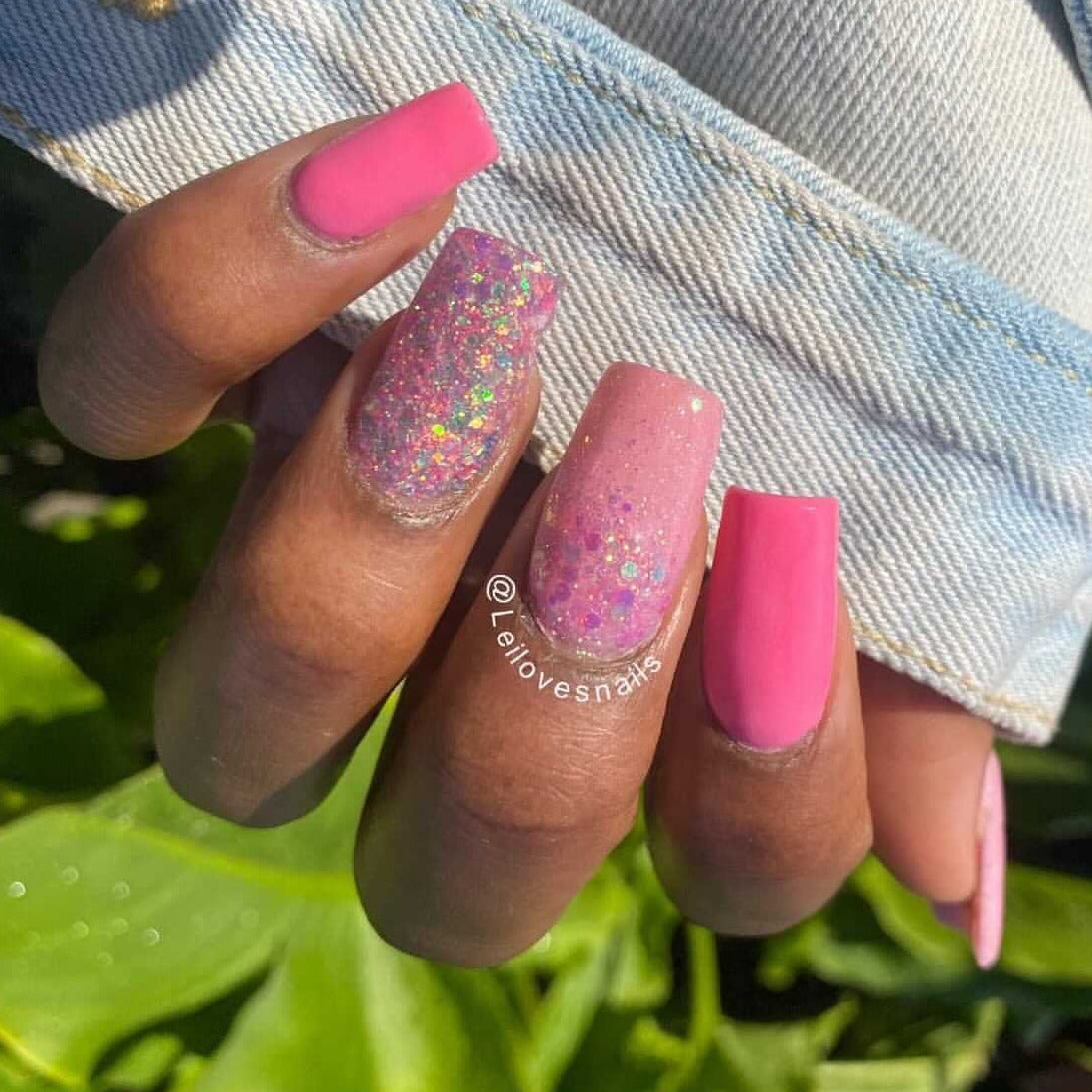 Pink solid and glitter dip powder nail polish on medium-length square nails with natural skin tone and denim jacket.