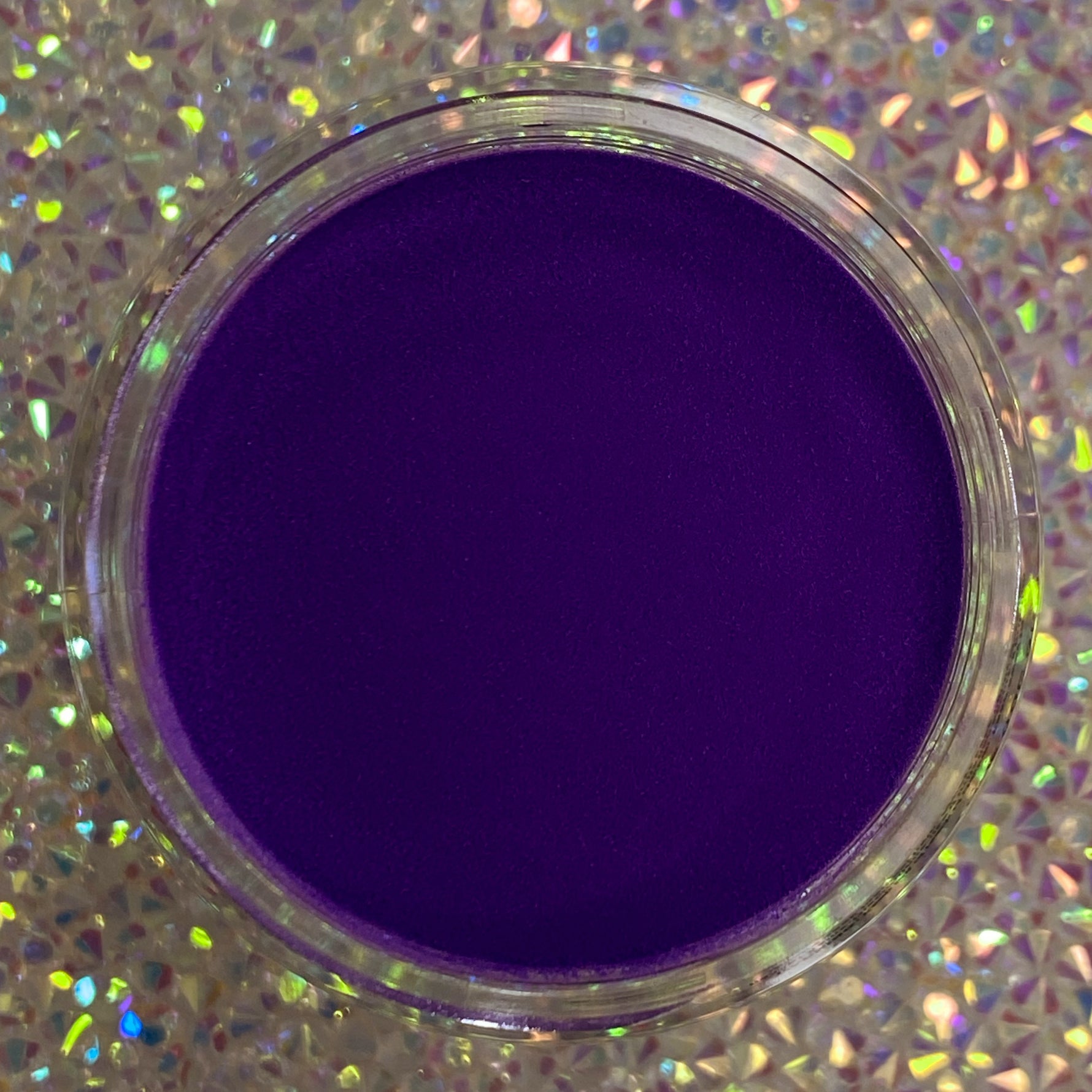 Deep purple solid dip powder in a clear round container against a holographic background.
