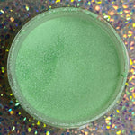 Open jar of fine mint green glitter dip powder with subtle shimmer on holographic background.