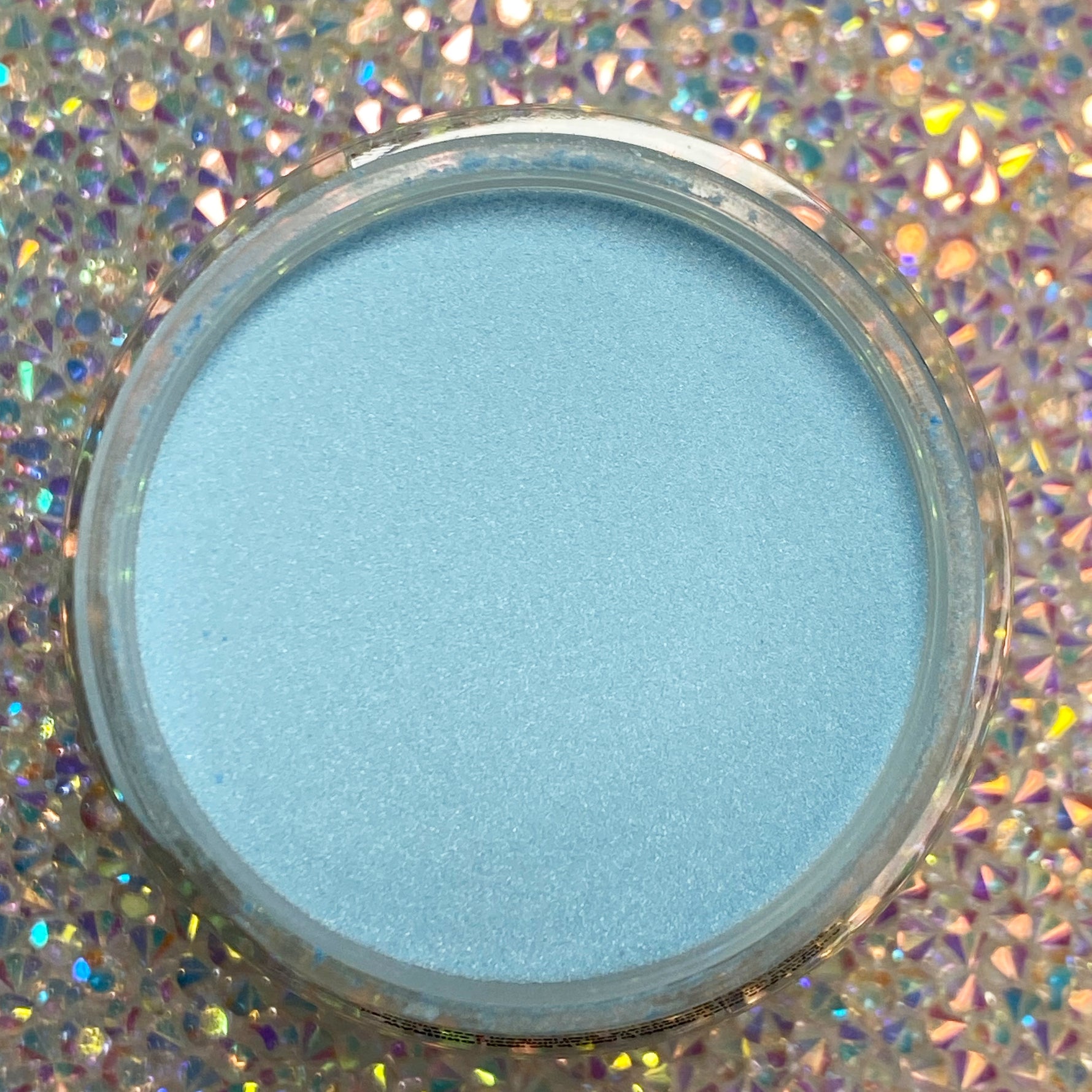 Open jar of fine, matte baby blue dip powder on holographic background.