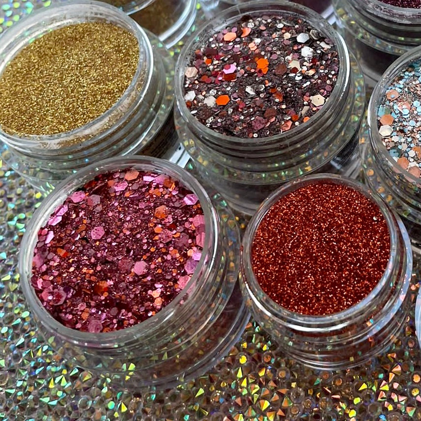 Open jars of chunky glitter dip powders in cranberry red, pink, gold, and multicolor hues.