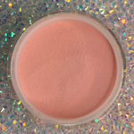 Round container of smooth peach-colored dip powder on iridescent holographic surface.