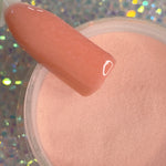 Coral peach dip powder nail polish swatch over matching loose powder with holographic sparkle background.