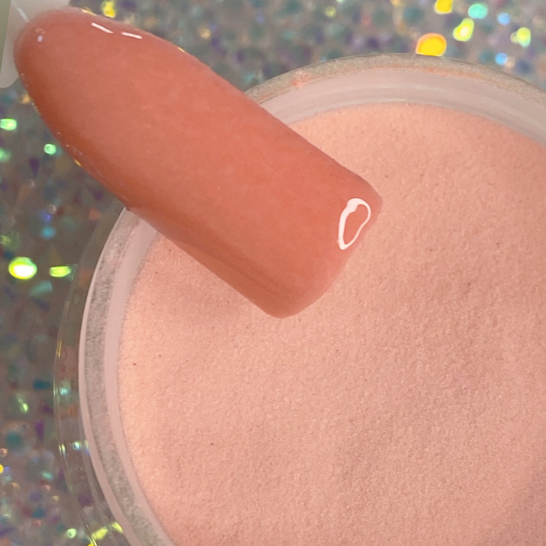 Coral peach dip powder nail polish swatch over matching loose powder with holographic sparkle background.