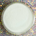 Milky white dip powder in clear round container on sparkly holographic background.