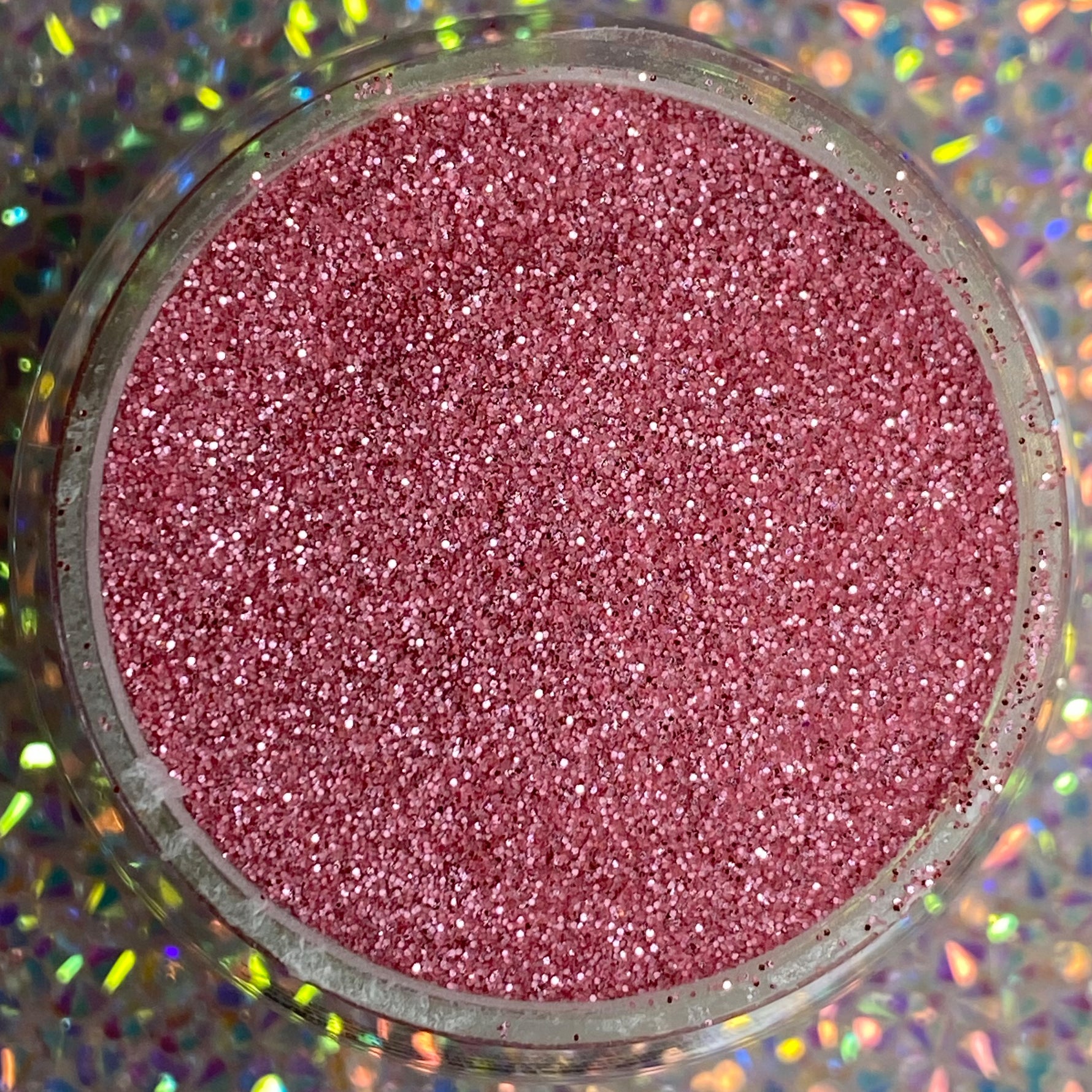 Fine rose gold glitter dip powder in round container on holographic background.