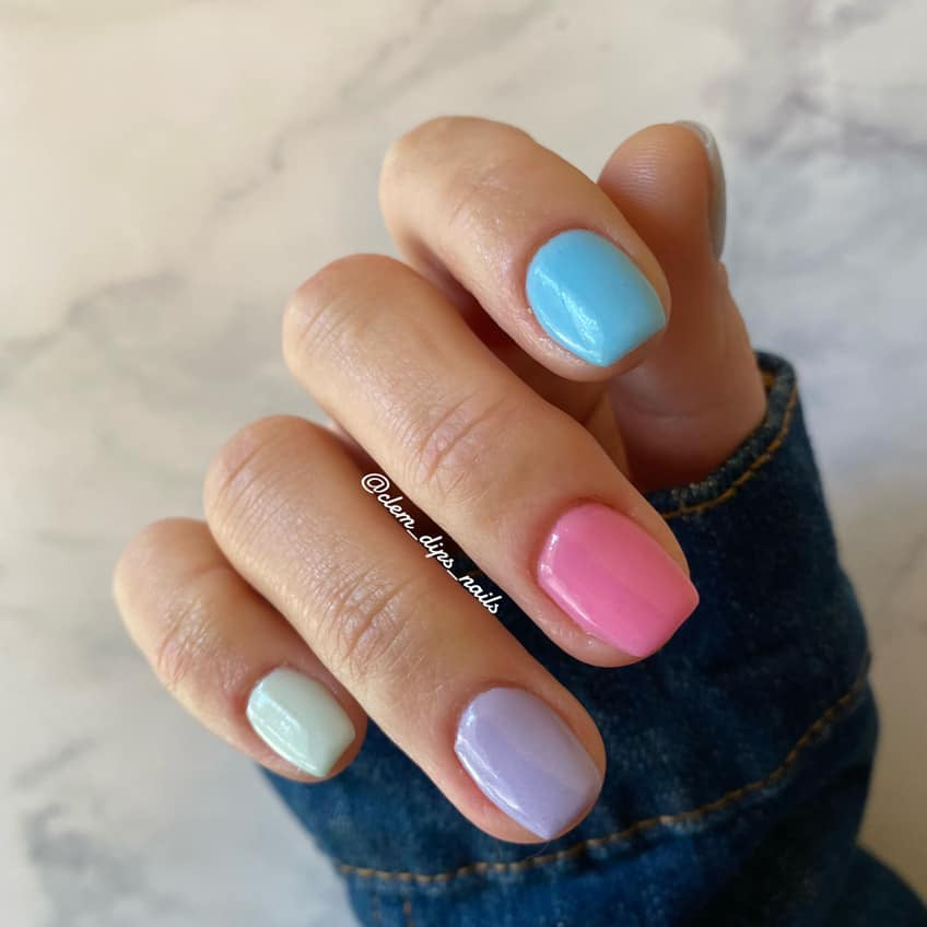 Hand with pastel blue, bright blue, pink, lavender, and mint green glossy nails against marble background.