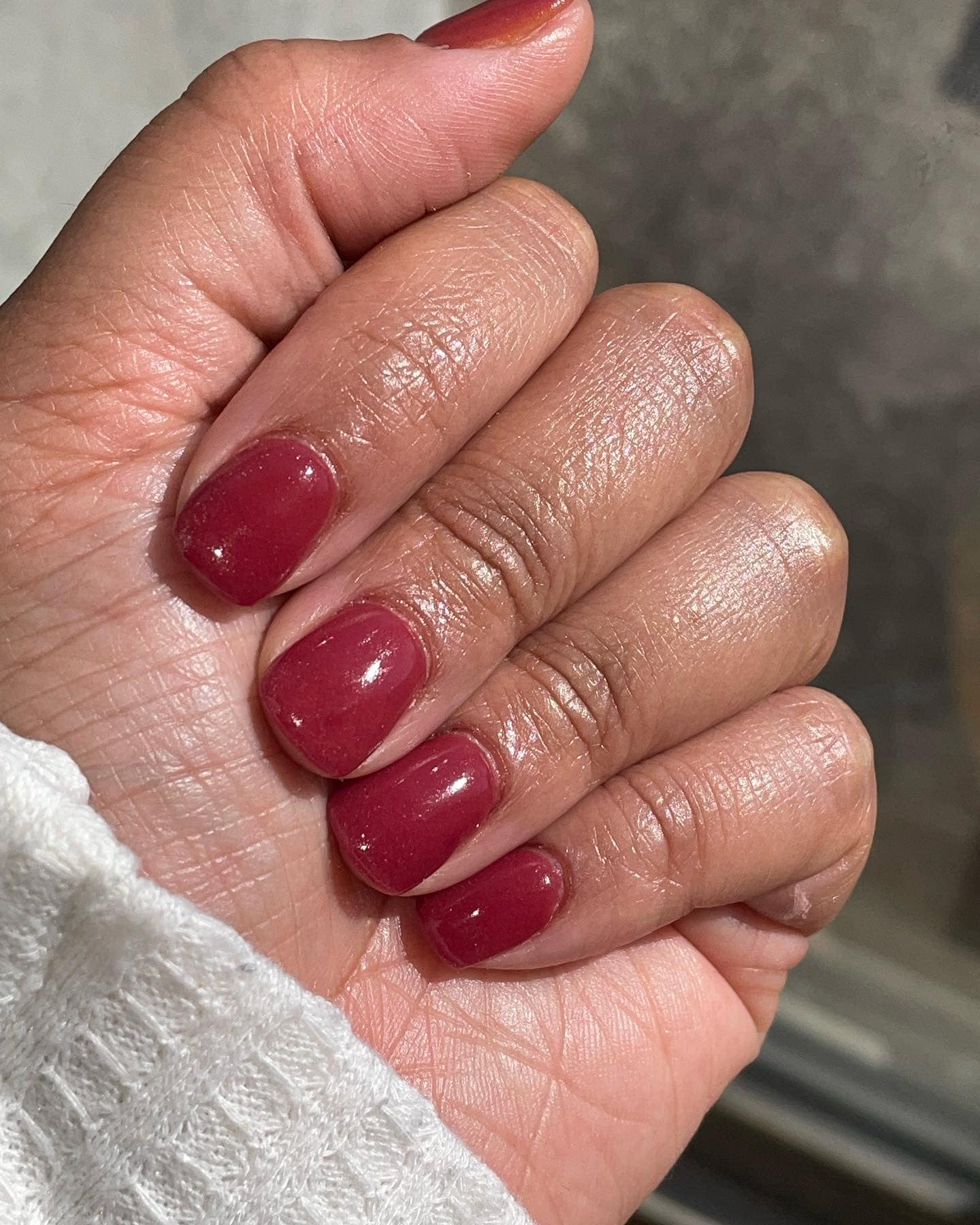 Short nails with glossy burgundy sun-changing dip powder polish on natural hand.