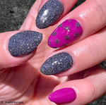 Black fine glitter nails with shiny reflective sparkle and one bright pink nail with black polka dots.