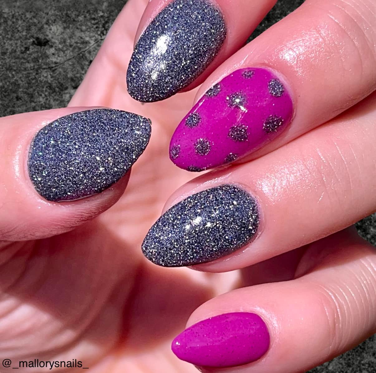 Black fine glitter nails with shiny reflective sparkle and one bright pink nail with black polka dots.