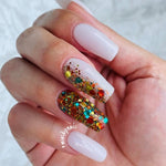 Glossy pale nude dip powder manicure with multicolored glitter accent nail on ring finger.