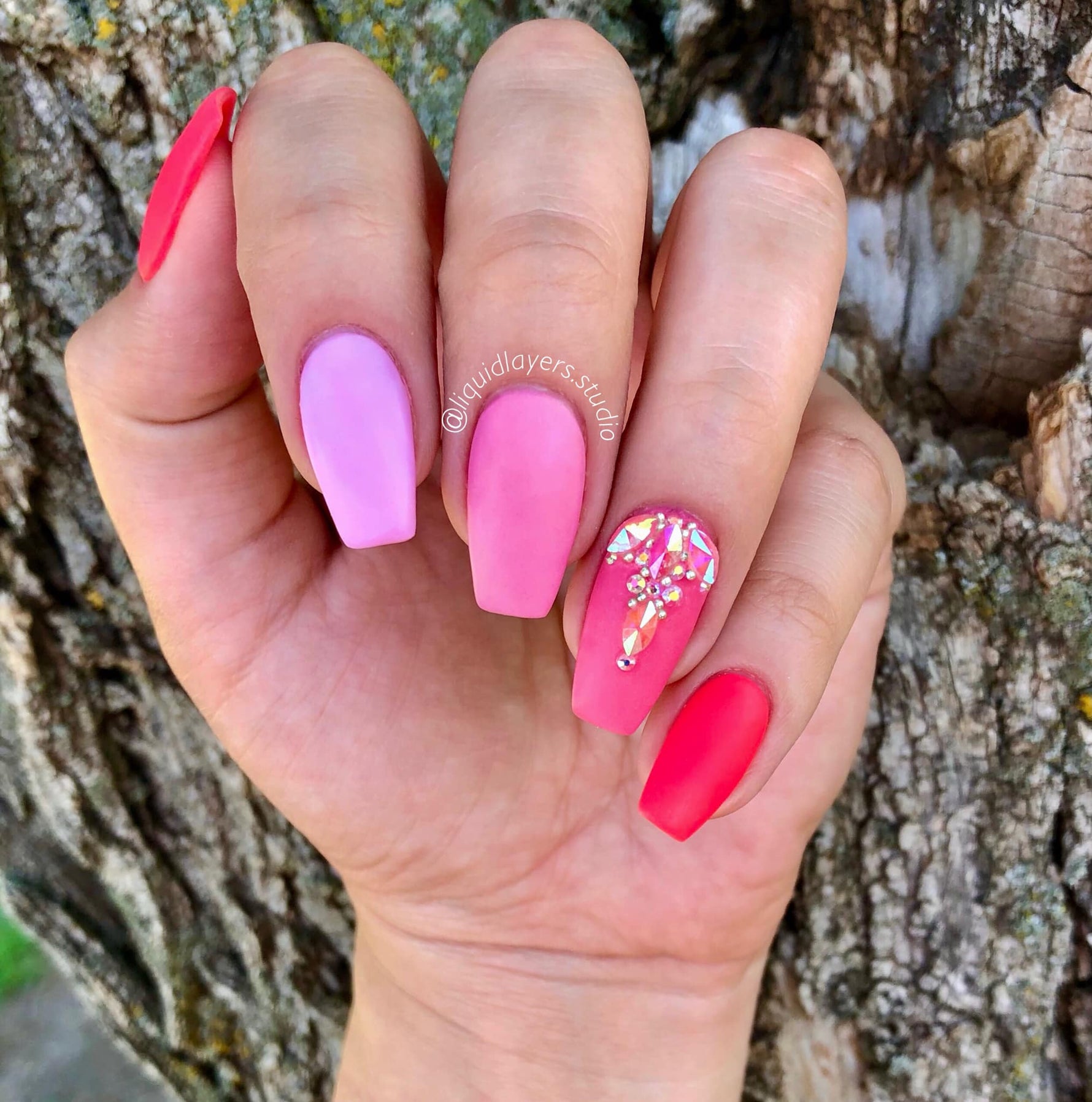 Hand with pink and coral matte nails, one accent nail decorated with gold flakes on ring finger.