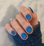 Teal blue nails with multicolor chameleon flake glitter on short square tips.