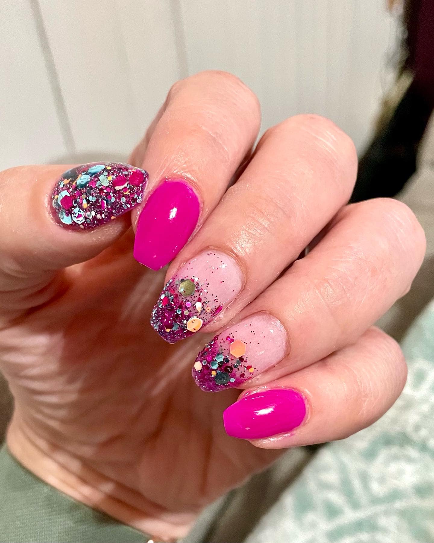 Bright pink nails alternating with clear nails featuring chunky multicolor glitter and large hexagonal glitter pieces.
