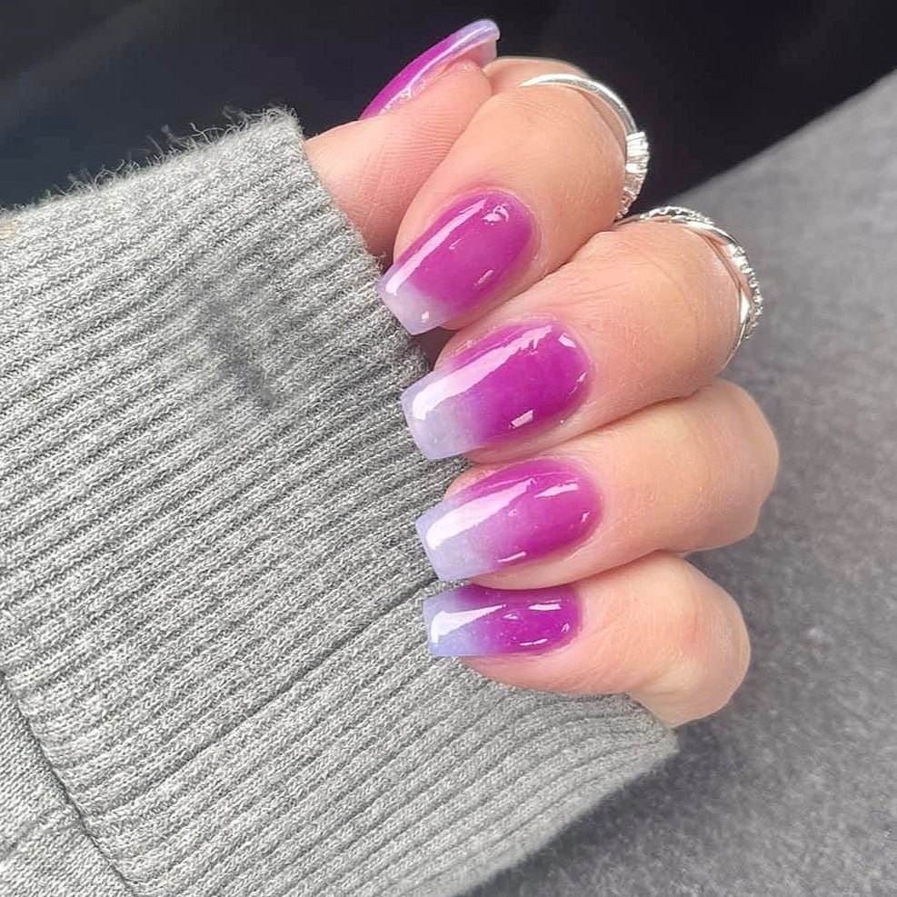 Purple to white ombre nails with a glossy finish and a subtle color shift, medium length square shape.