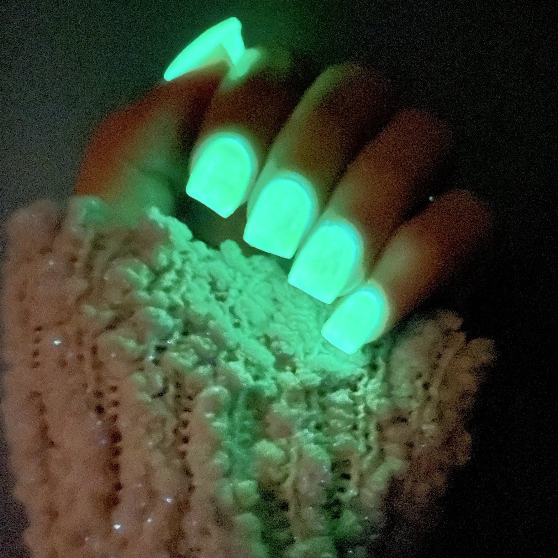 Glowing neon green squared nails on hand with textured pink fabric background.