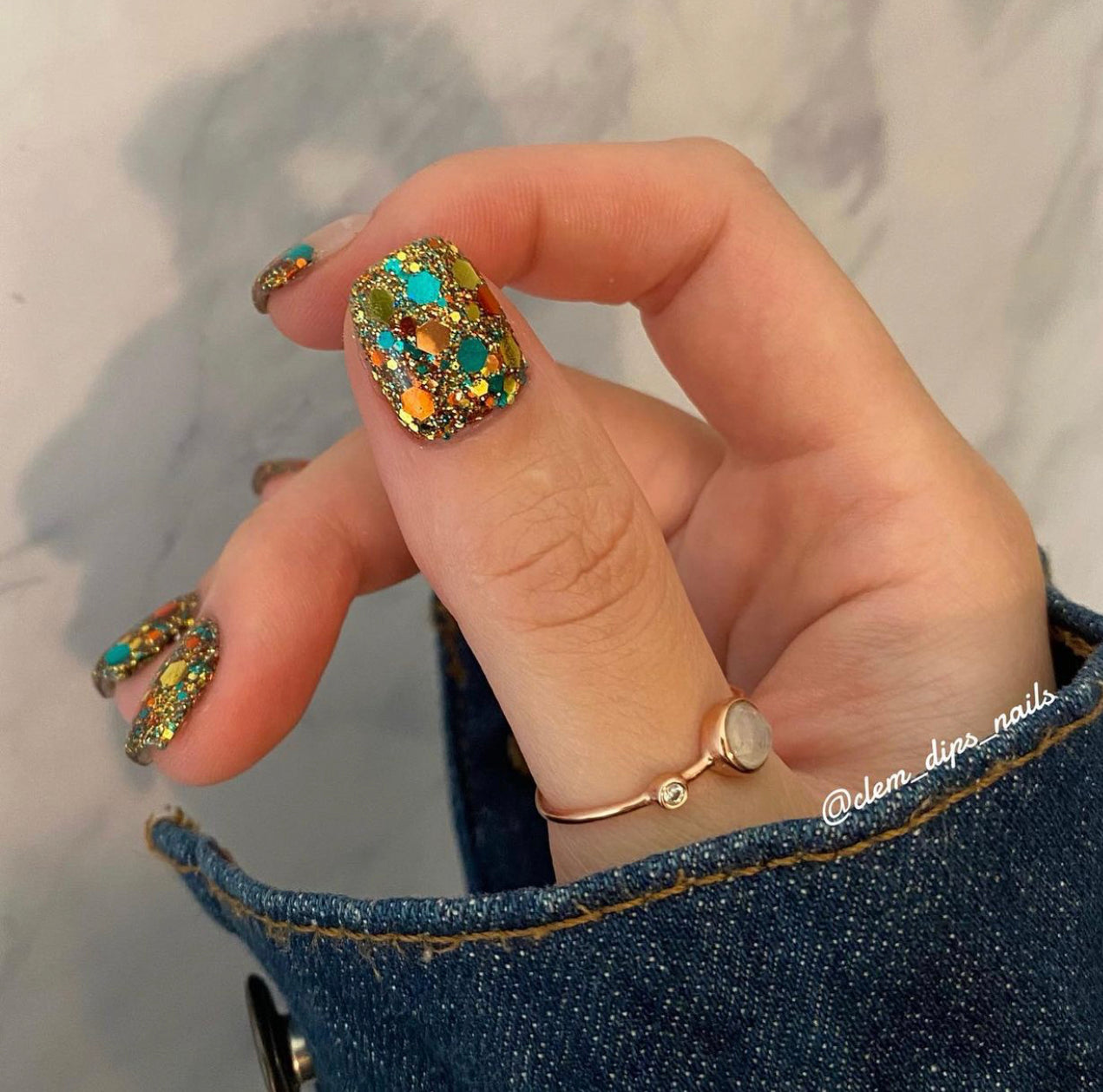 Chunky multicolor glitter nail polish with blue, orange, yellow accents on short nails.