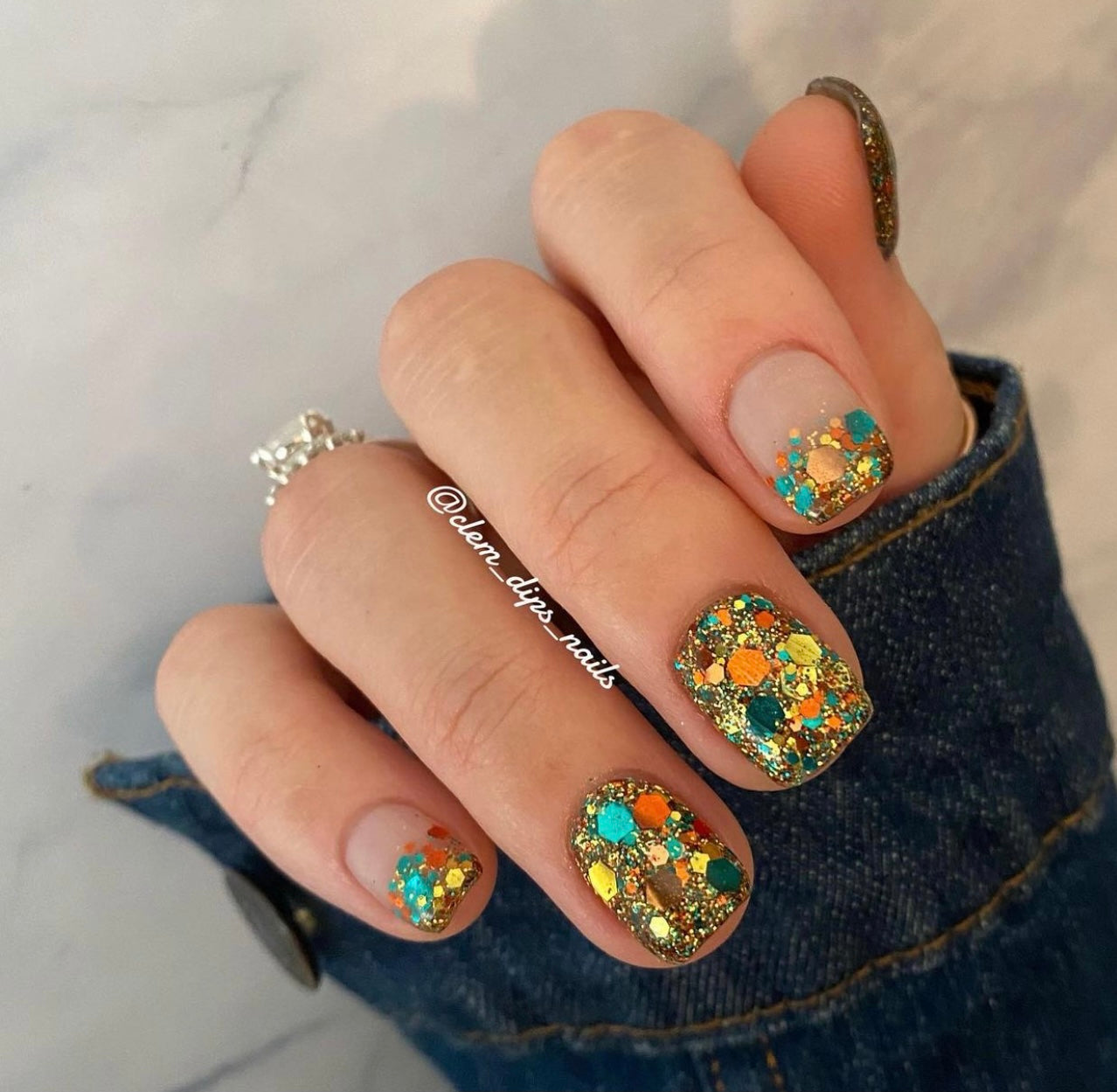 Multicolor chunky glitter nail dip with blue, yellow, and orange accents on short nails.