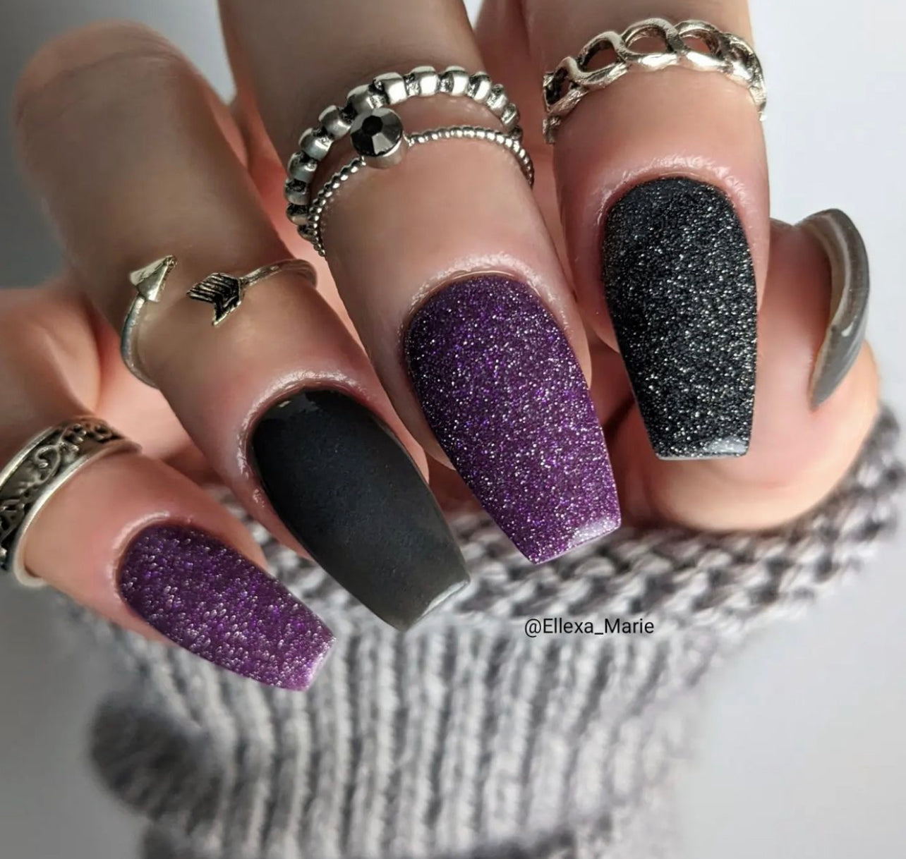 Manicure with matte black, purple glitter, and black fine glitter nails, adorned with silver rings.