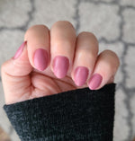 Soft muted pink matte nails on medium-length oval-shaped fingers with a black sleeve background.