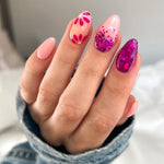 Pink to wine color-changing almond nails with floral and glitter accents on hand with denim sleeve.