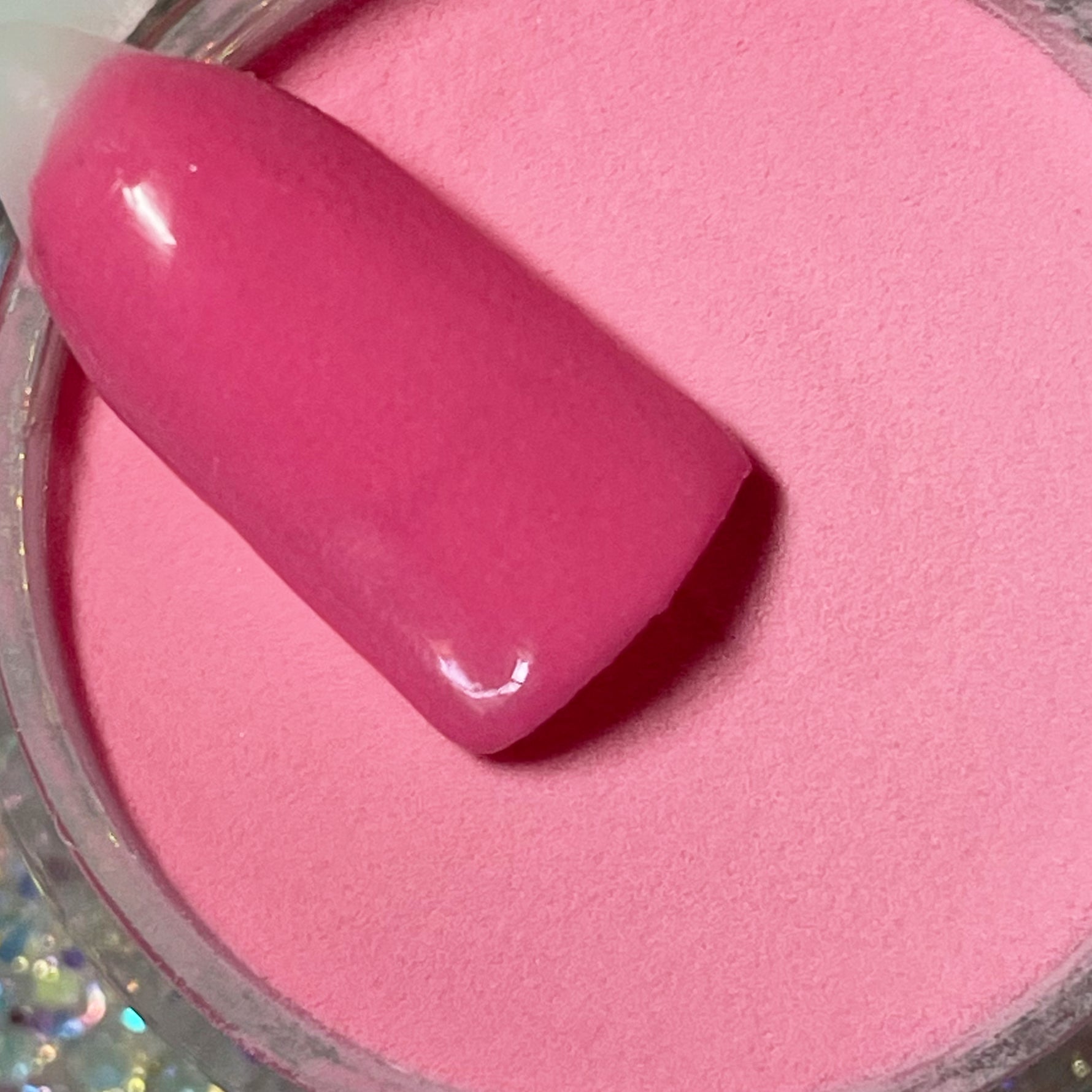 Bright pink solid dip powder with glossy nail swatch sample over open jar.