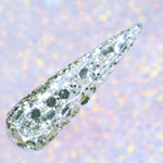 Clear nail tip coated with chunky silver glitter in various sizes against a soft iridescent background.