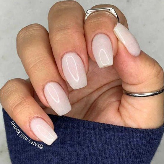 Pale pink square nails with subtle shimmer on a hand wearing silver rings and a blue sleeve.