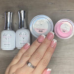 Hand with French tip pink dip powder nails beside active and base coat bottles and dip powder containers on wood background.
