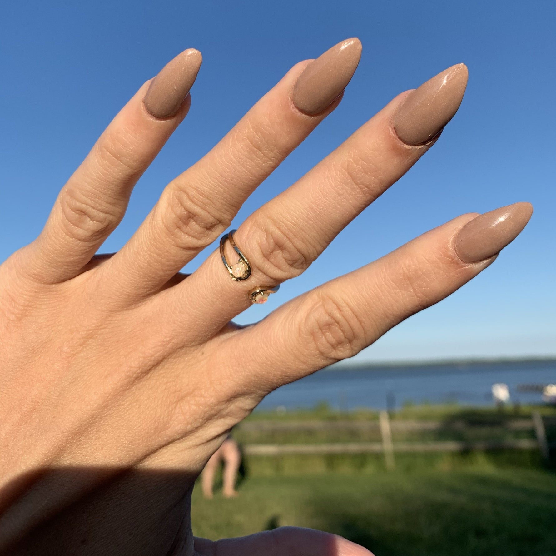 Almond-shaped nails with smooth, glossy tan nude polish against a clear blue sky background.