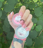 Hand with pink French tip nails holding two small clear containers of dip powder labeled FT48 Delightful and 