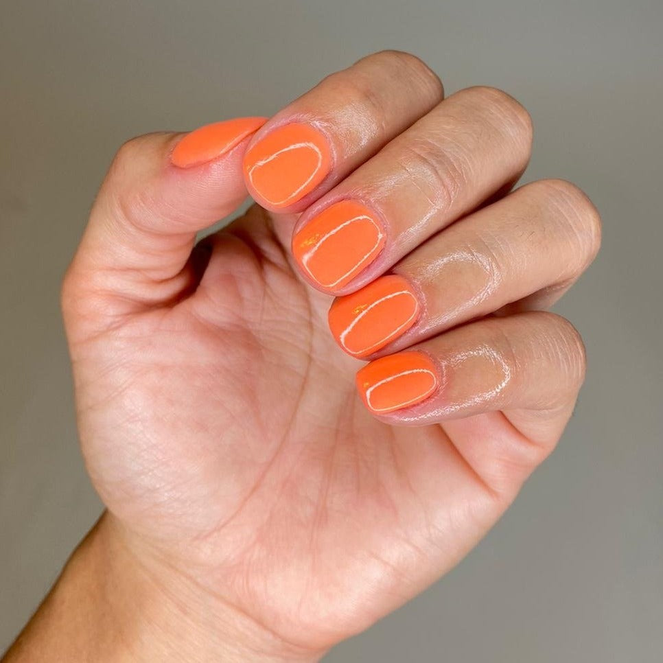 Hand with medium-length nails painted in vibrant glossy orange dip powder polish.