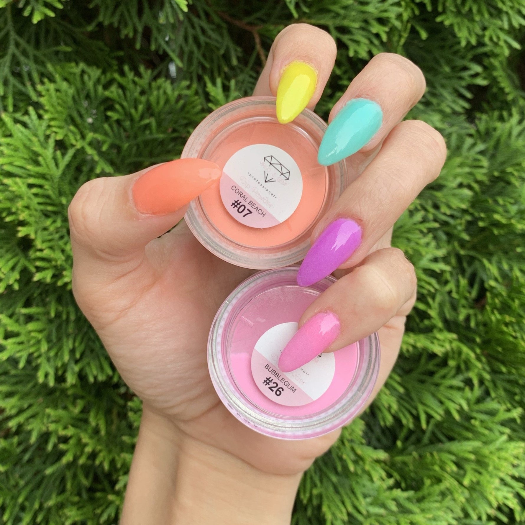 Hand with pastel coral orange, yellow, turquoise, purple, and pink dip powder nails holding coral and pink dip powder jars.